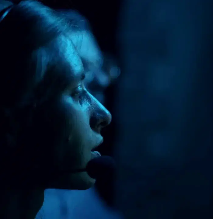 An operations analyst wearing a headset, lit blue by the monitors she is watching